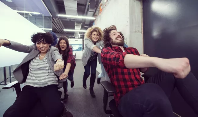 Equipo joven de profesionales se divierte con sillas de oficina en un espacio de trabajo informal de estilo coworking