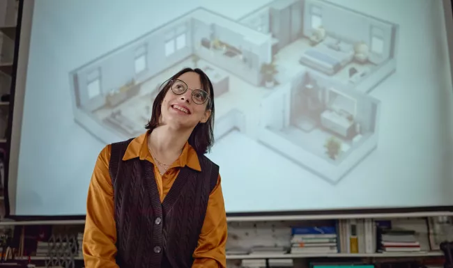 Mujer con gafas sonriendo y mirando hacia arriba delante de una pantalla con la proyección axonométrica de una vivienda