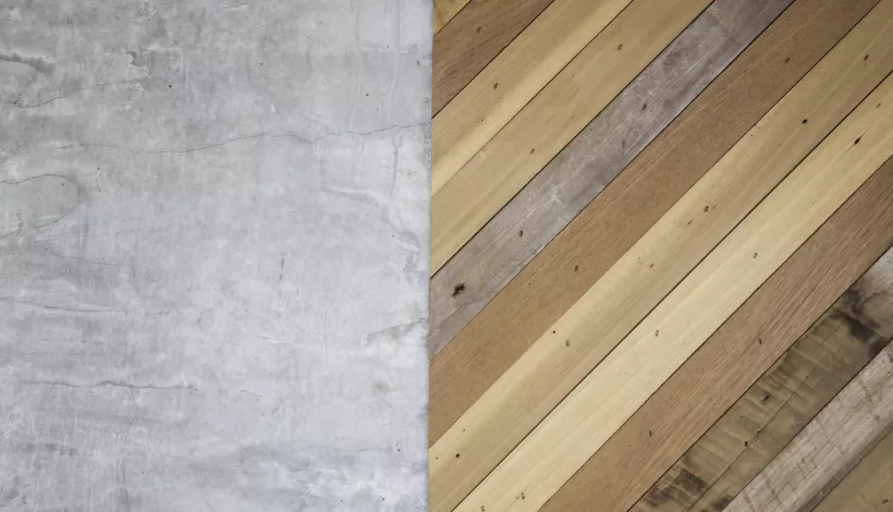 Detalle de pared dividida entre hormigón visto y lamas de madera diagonal, representando la comparativa entre los dos materiales clave de la construcción sostenibl