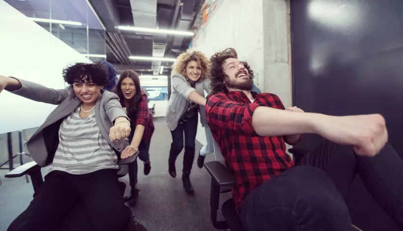 Equip jove de professionals es diverteix amb cadires d'oficina en un espai de treball informal d'estil coworking