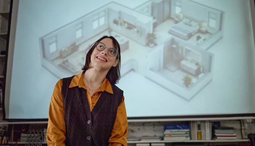 Mujer con gafas sonriendo y mirando hacia arriba delante de una pantalla con la proyección axonométrica de una vivienda