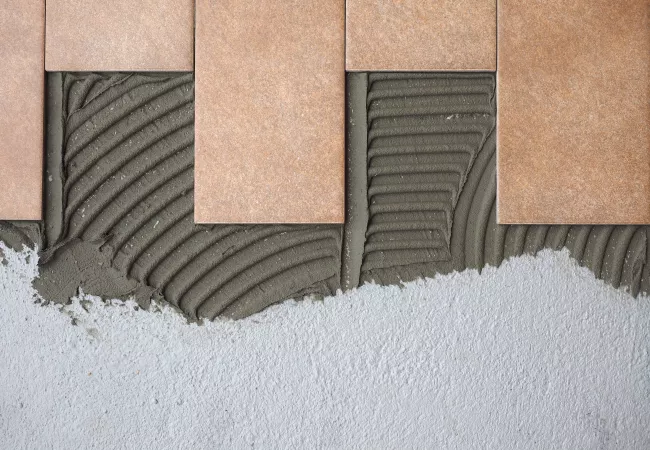 Proceso de instalación de azulejos cerámicos con mortero adhesivo, mostrando materiales técnicos de construcción que requieren estrategias específicas para el cierre de su ciclo de vida sostenible.