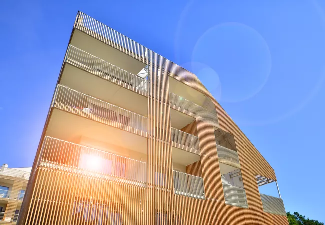 Edificio residencial de varias plantas con fachada de lamas de madera y balcones, ejemplo de construcción sostenible en altura media