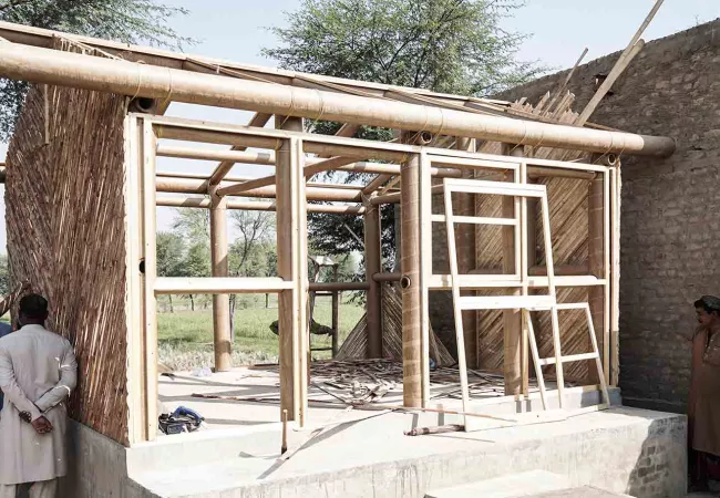 En marzo de 2025, Shigeru Ban Architects y su Voluntary Architects' Network completaron dos viviendas piloto en el distrito de Dadu (Sindh, Pakistán), uno de los más devastados por las inundaciones de 2022 que afectaron a un tercio del país. Las casas se construyen con bambú y caña —materiales locales y disponibles— sobre una plataforma elevada de hormigón, en colaboración con la organización local Safe Delivery Safe Mother y con participación directa de las familias receptoras. El proyecto ilustra el princ