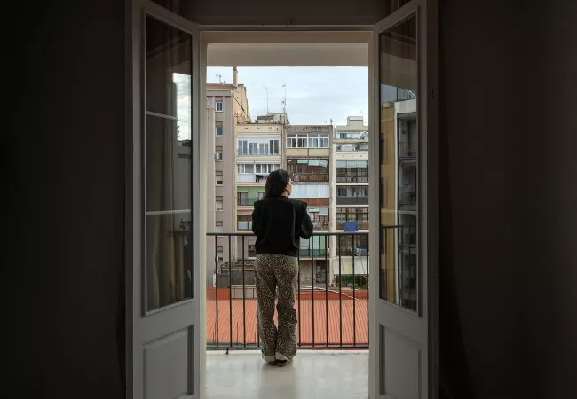 Dona d'esquena en un balcó mirant les façanes posteriors i les galeries d'un interior d'illa de l'Eixample.
