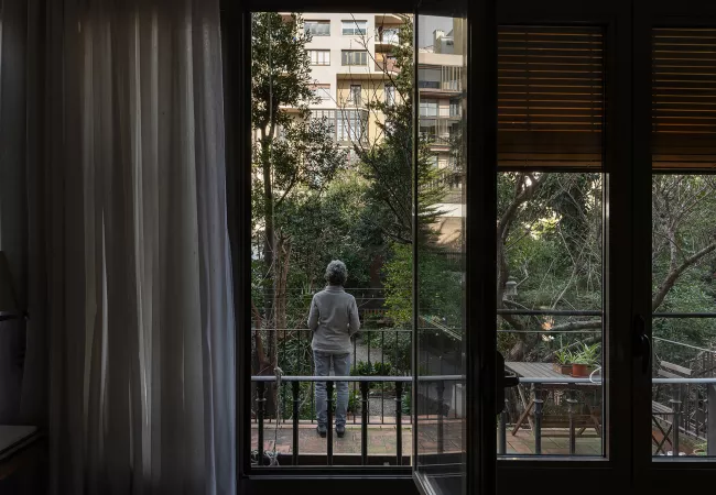 Persona d'esquena en un balcó mirant cap a un interior d'illa enjardinat de l'Eixample, ple d'arbres i vegetació.
