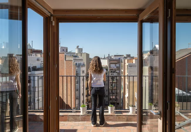 Dona d'esquena en una terrassa mirant els terrats i les façanes de l'Eixample de Barcelona sota un cel blau.