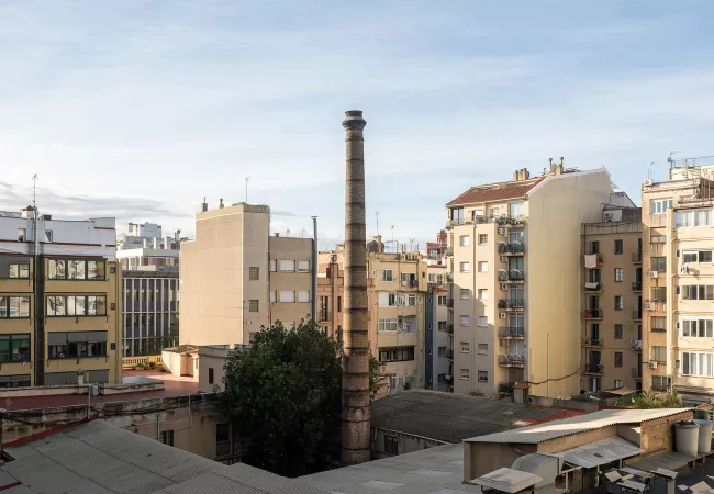 Xemeneia de maó de l'antiga Fàbrica Lehmann, dempeus a l'interior d'illa de l'Eixample, envoltada de terrats i edificis d'habitatges.