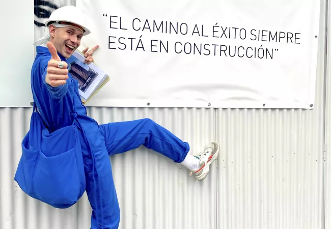 L'Erik Harley disfressat d'obrer davant d'una lona amb el lema «El camino al éxito siempre está en construcción»