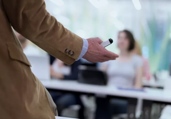 Docente con rotulador dirigiéndose a los alumnos durante una clase presencial.