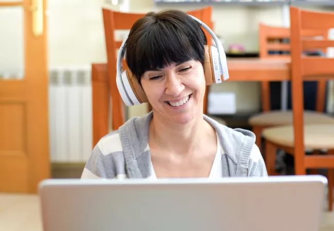 Mujer con auriculares sonriendo mientras sigue una sesión online en su portátil
