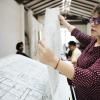 Arquitecta revisando planos en una mesa de trabajo en un estudio de arquitectura con equipo al fondo.